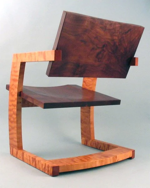 A modern, minimalist wooden chair with a curved frame and a dark wood backrest, set against a plain background.