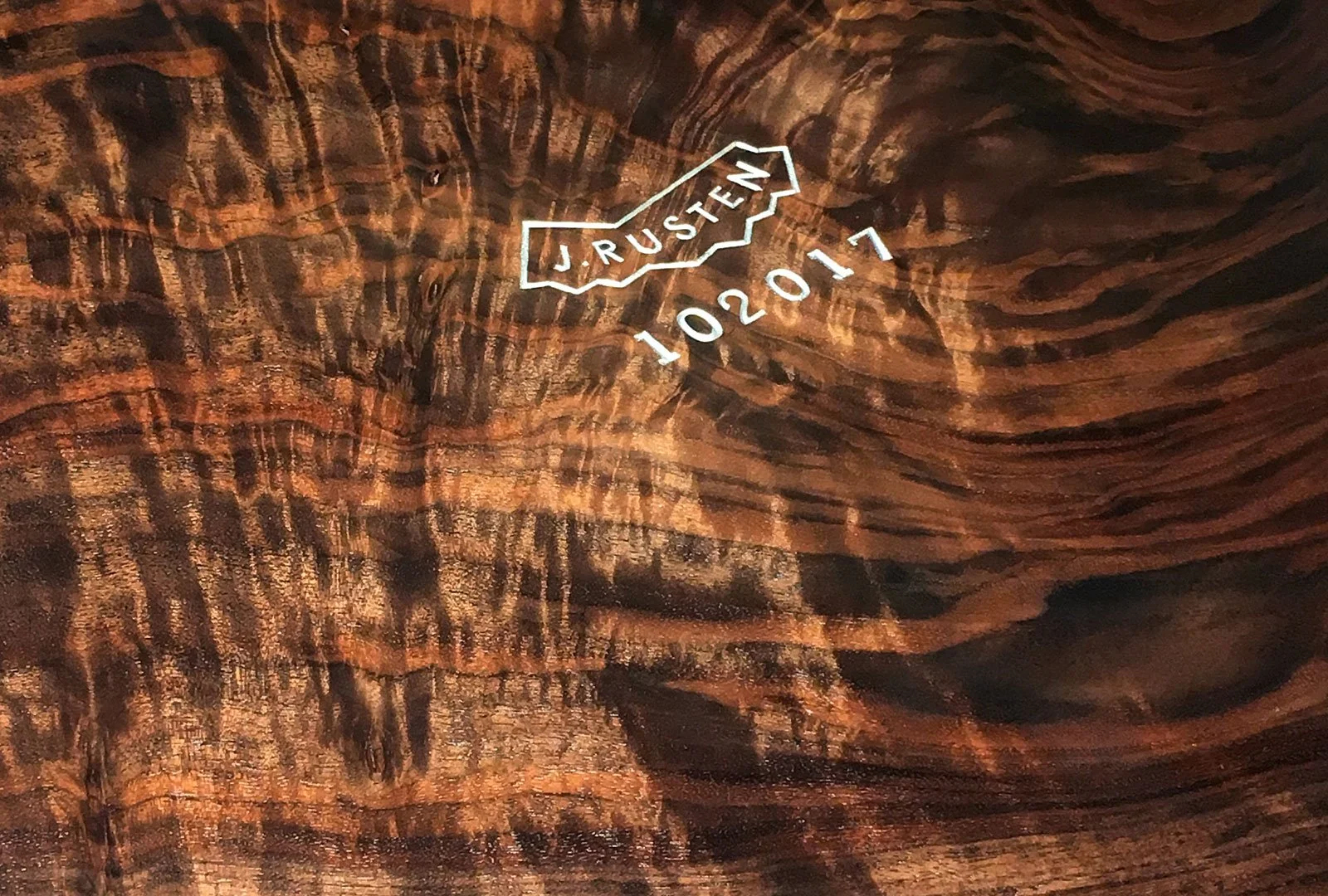 Close-up of textured, layered, reddish-brown rock surface with a neon sign that reads 'RUSTEN 102017' and a directional arrow pointing to the right.