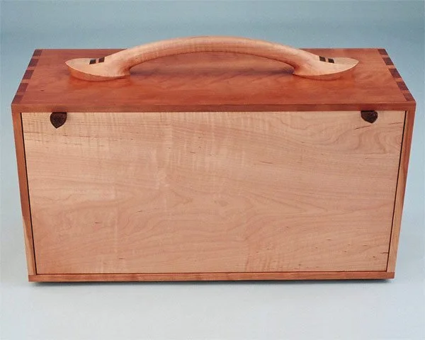 A wooden storage chest with a handle on top, made of light and dark wood, against a light background.