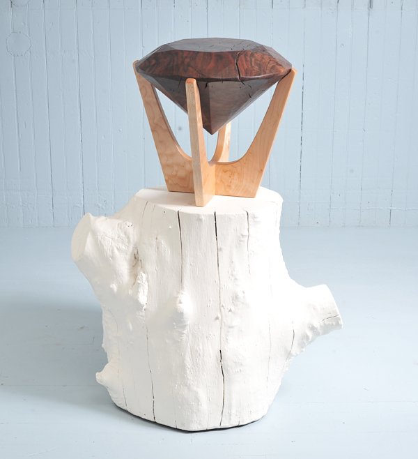A sculptural piece with a white, textured wooden base resembling a tree trunk and a geometric wooden bowl supported by three wooden prongs on top.