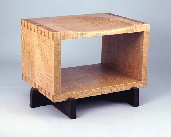 A wooden open-fronted side table with a rectangular shape and black angled legs against a plain light background.