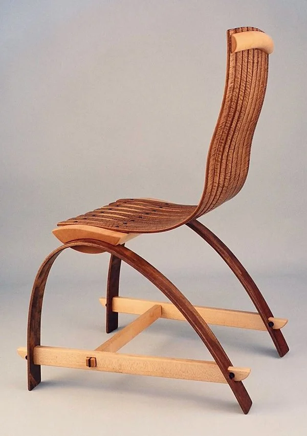 A miniature wooden rocking chair with a curved backrest and seat, made of alternating dark and light wood, on a light background.