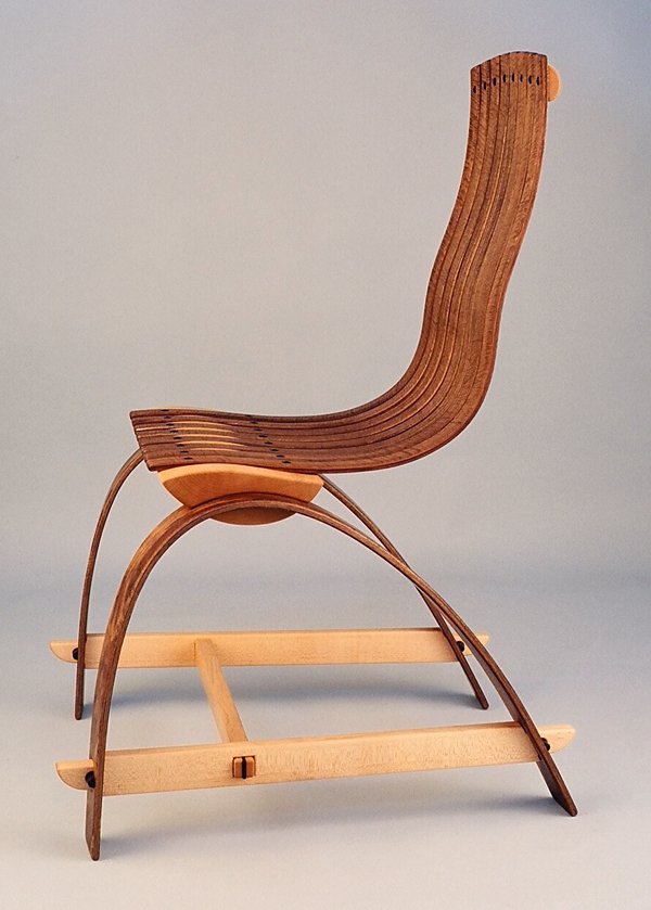 A miniature wooden rocking chair with curved armrests and a slatted backrest, placed on a flat surface against a plain background.