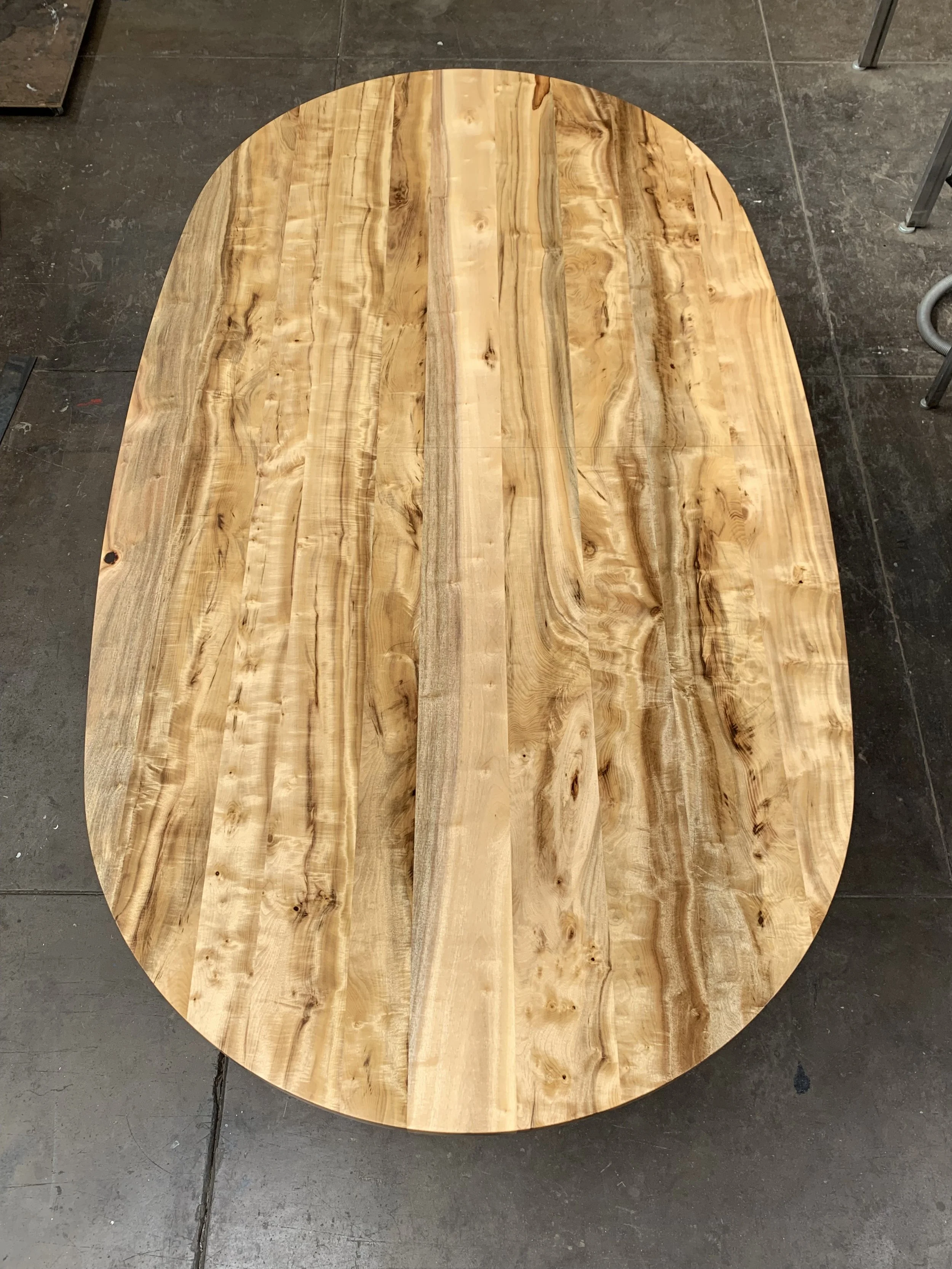Round wooden table with a natural wood finish and visible grain patterns, set on a dark tiled floor.