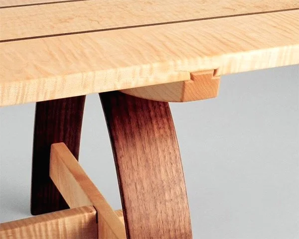 Close-up of a wooden table with a light-colored top and dark-colored angled legs.