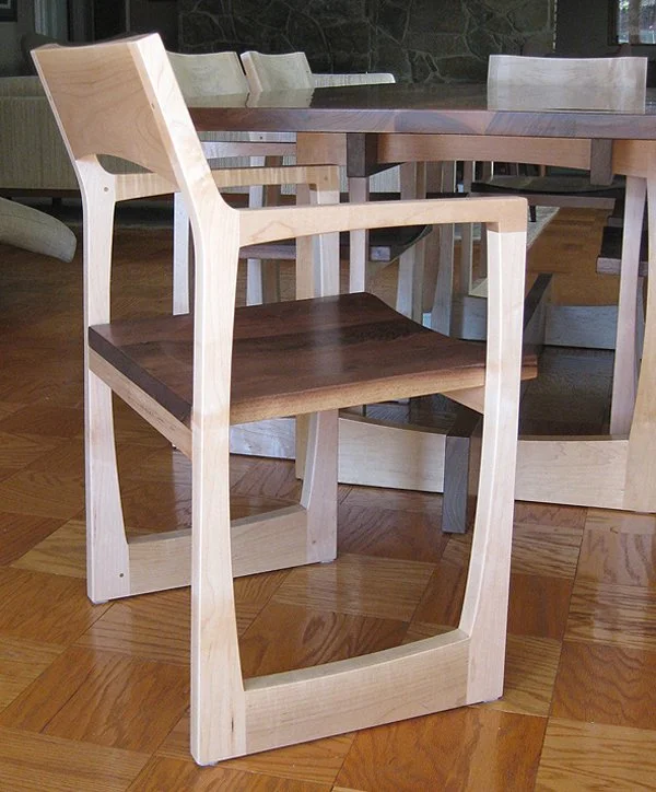 Wooden dining chair with light frame and dark seat sitting on a hardwood floor in a dining room.