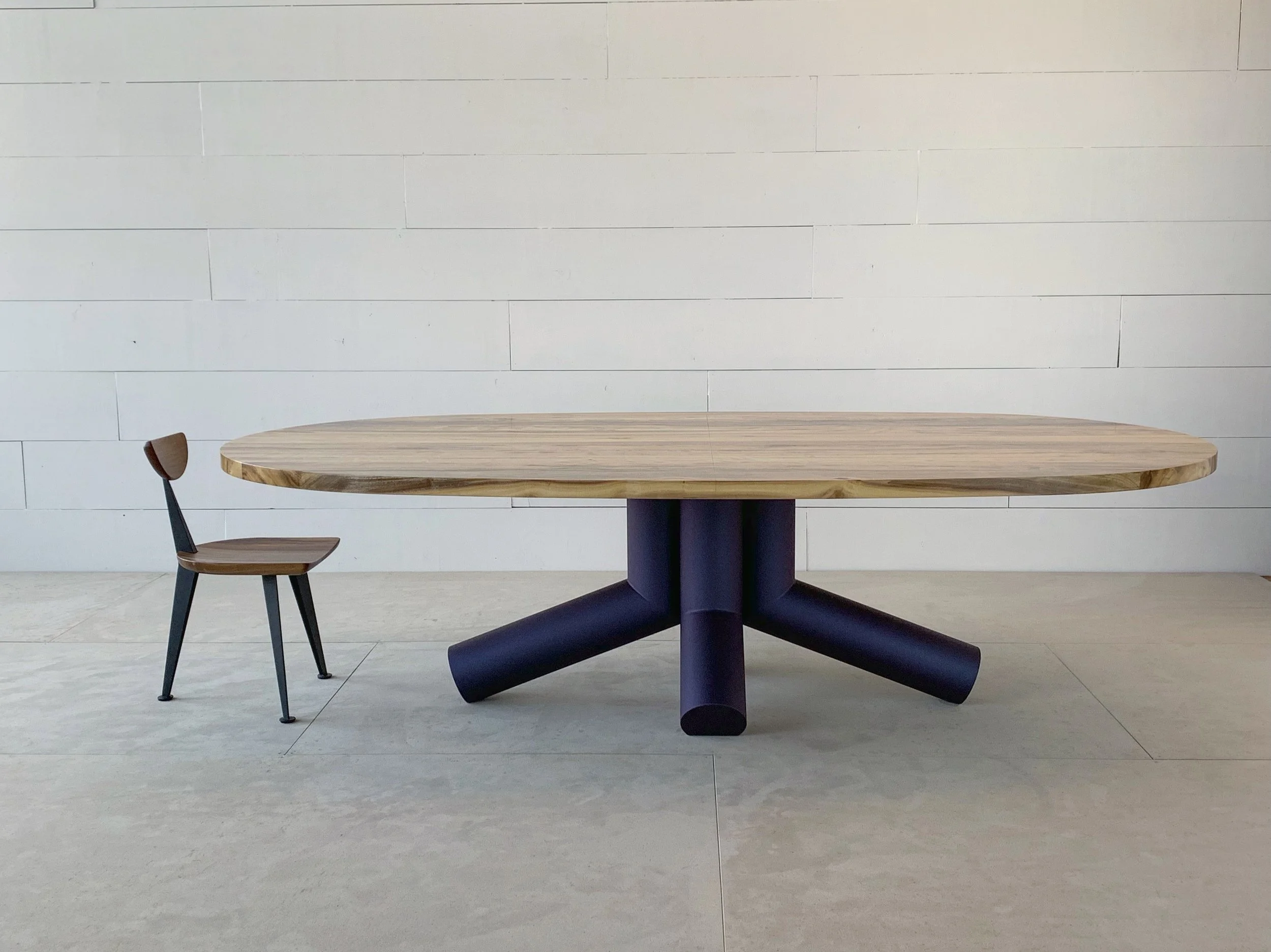 A wooden table with a black base and two wooden chairs against a white tiled wall.