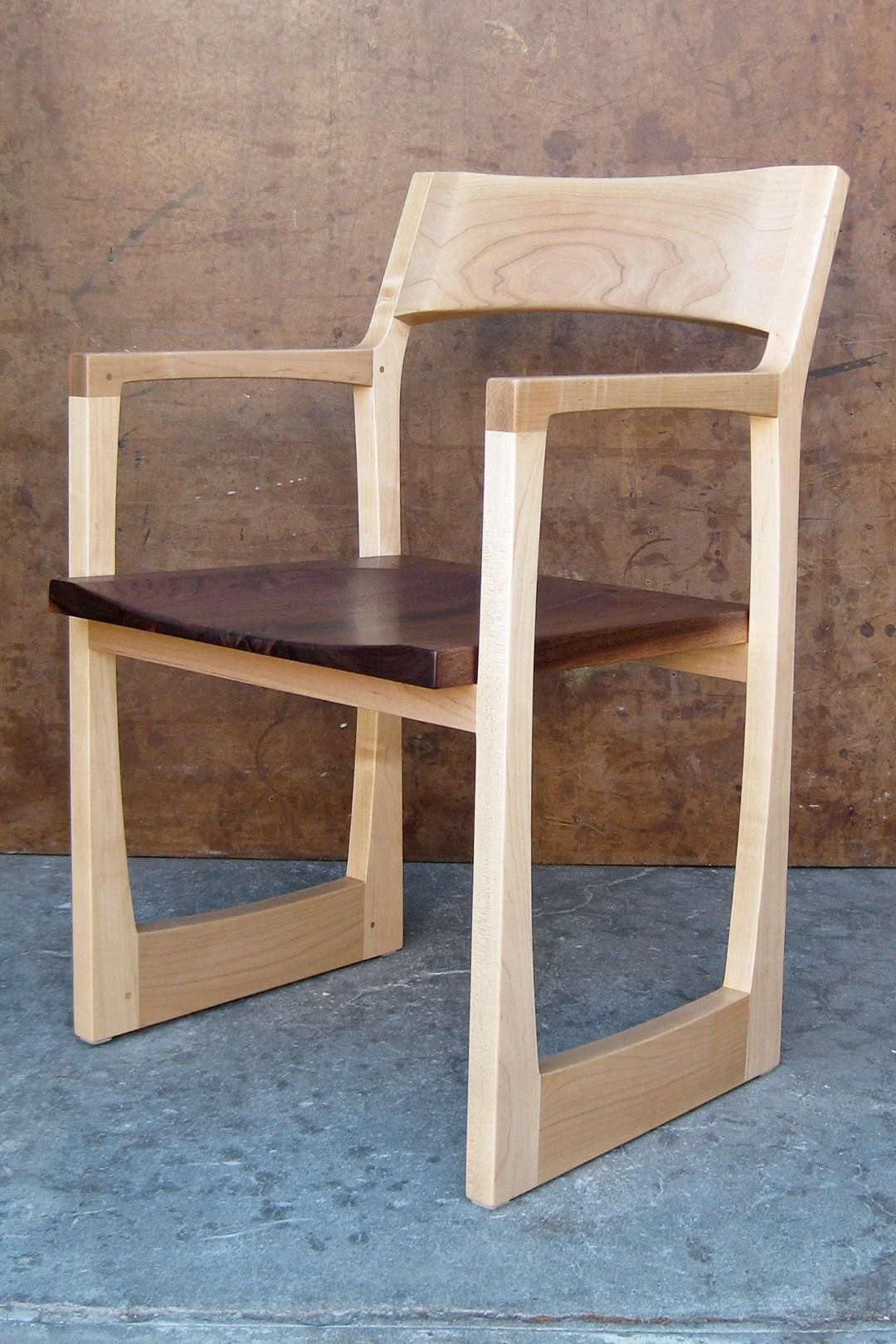 A modern wooden chair with a dark wooden seat and light wooden frame, set against a textured brown background.