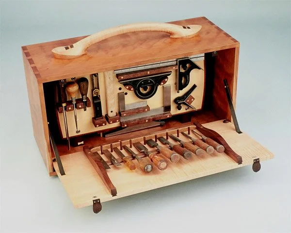 A wooden mechanical music box with a handle on top, featuring a set of tuned metal bars, gears, and levers inside.