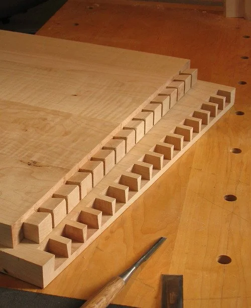 A wooden workbench with woodworking tools and partly assembled wooden pieces with evenly spaced rectangular notches.