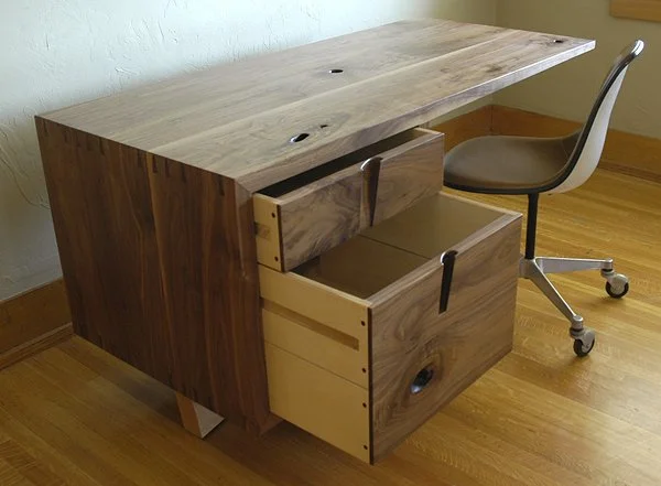 Wooden desk with two open drawers and a rolling office chair in a room with hardwood flooring.