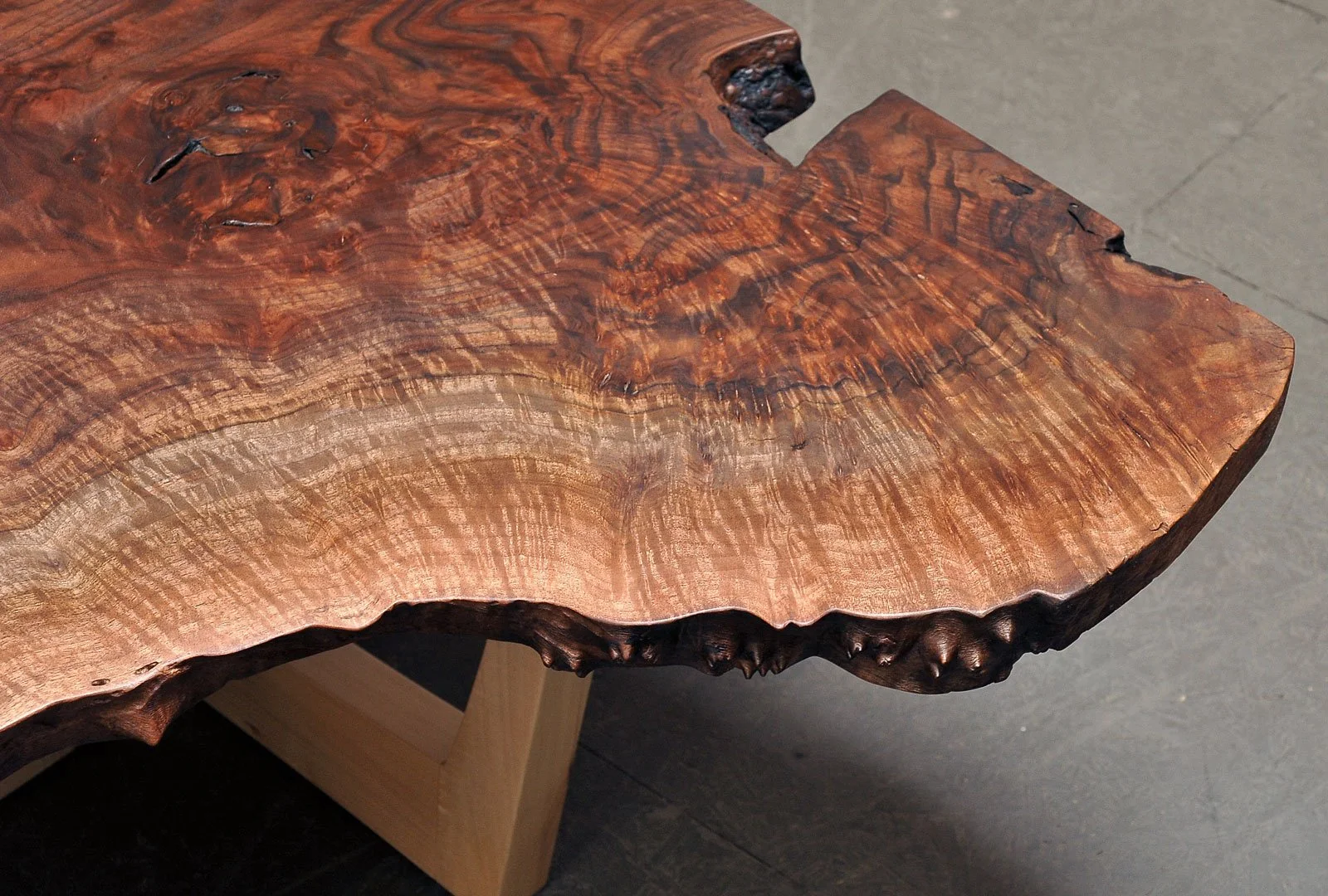 Close-up of a polished wooden table with a live edge, showing natural grain, knots, and irregular edges.