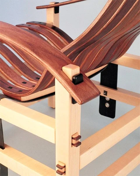 Close-up of a wooden chair with a curved seat and backrest, showcasing the craftsmanship and joinery details.
