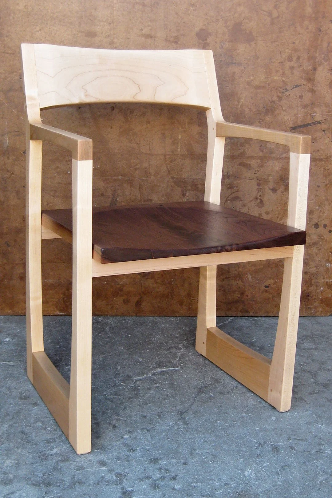 A modern wooden chair with a light-colored frame and dark wooden seat, set against a textured brown background.