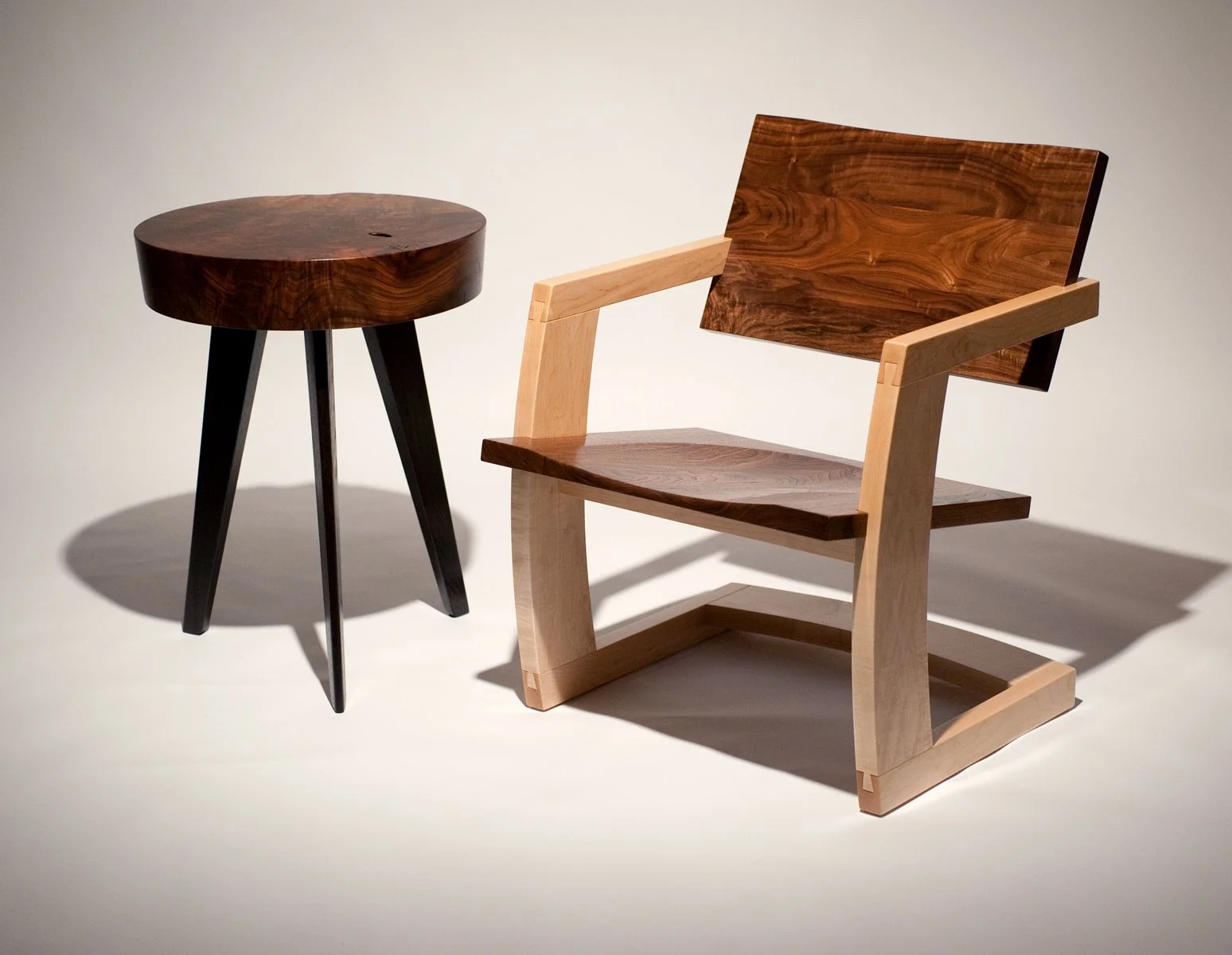 Three wooden furniture pieces: a dark wood round side table with black legs, and a light wood armchair with a darker wood backrest and seat.