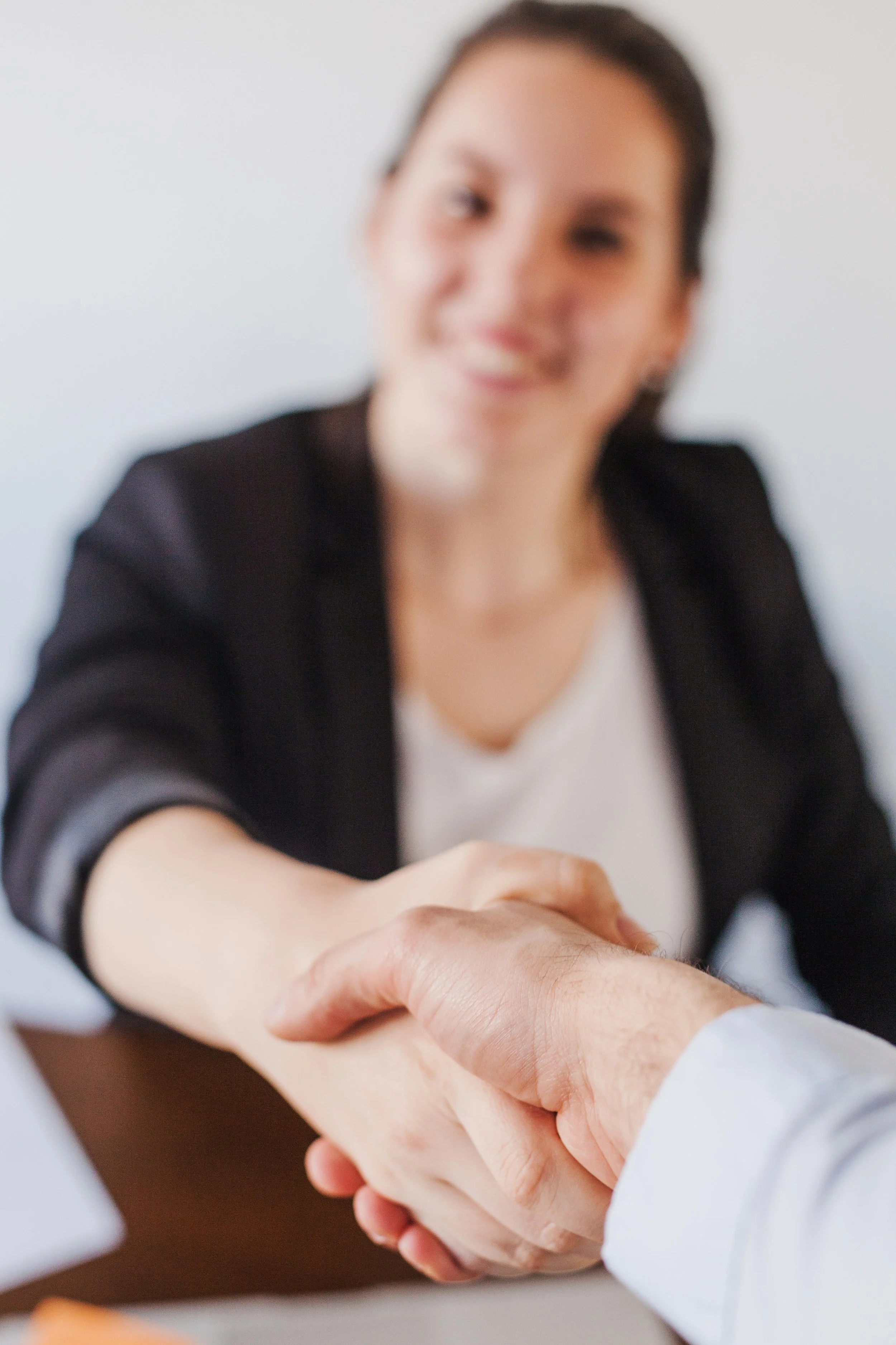 A woman smiling and shaking hands with another person in a professional setting.