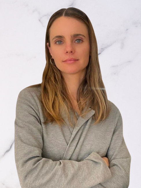 A woman with long light brown hair wearing a gray sweatshirt standing with arms crossed against a white marble background.