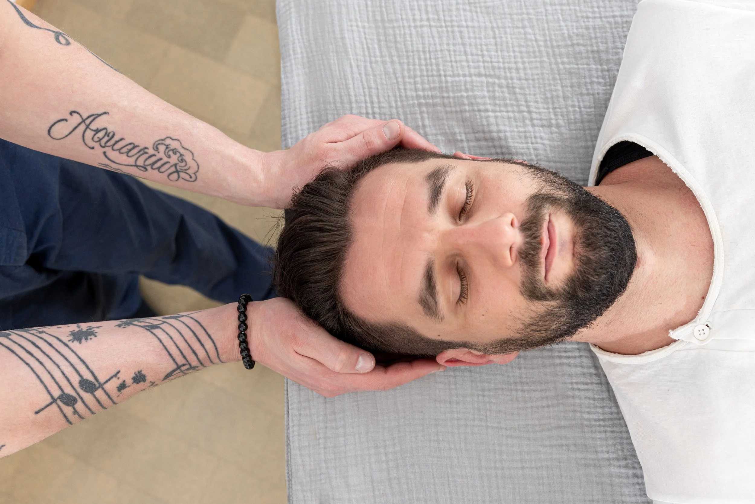 Ein Mann liegt entspannt auf einer Massagebank, während jemand seinen Kopf und Nacken massiert.