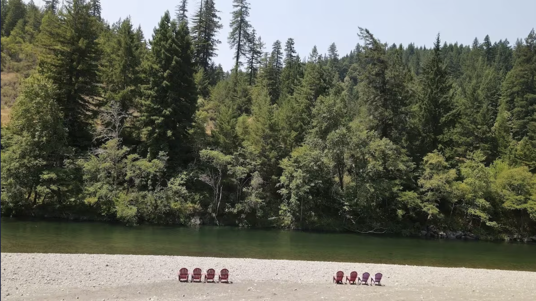 Beach with colorful Adirondack chairs facing a forested hillside.