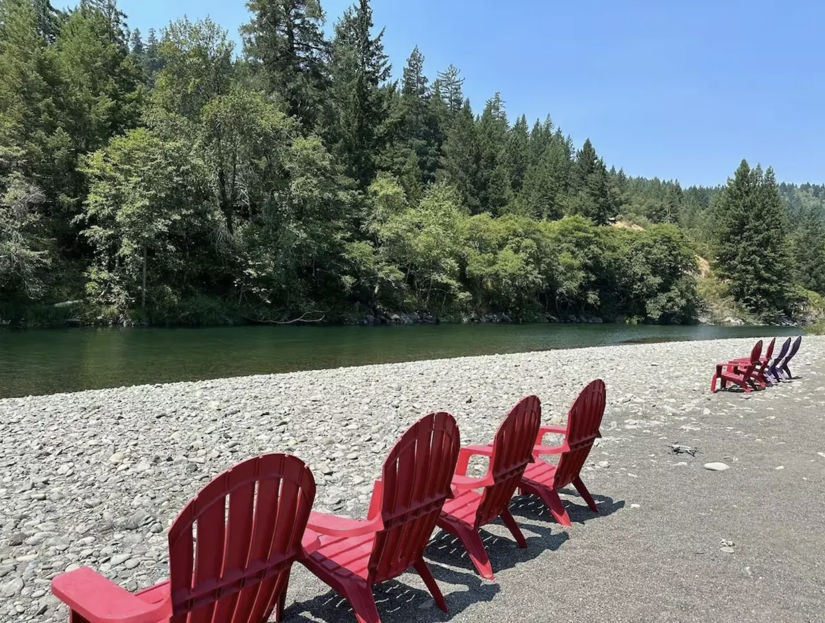 Red and purple chairs facing a river with forested hills and a clear blue sky in the background.