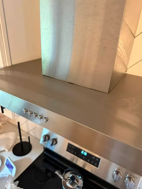 Close-up of a stainless steel kitchen stove and range hood with control knobs.