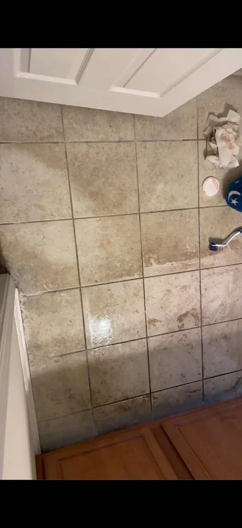 Dirty kitchen floor with wet spots, a sink faucet, cleaning supplies, and a cabinet with a door.