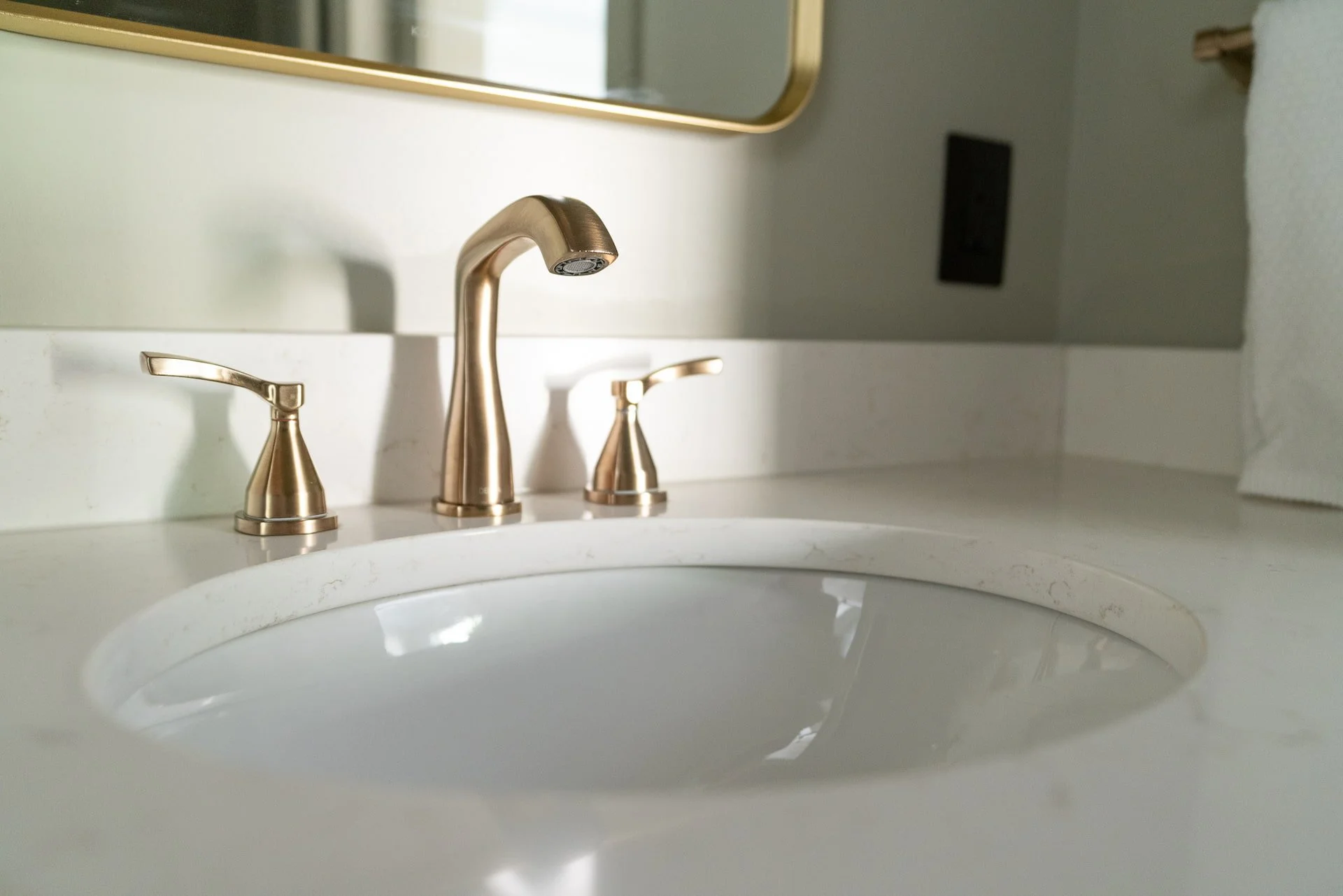Close-up of a bathroom sink with a gold-colored faucet and handles, reflecting light onto the white countertop.