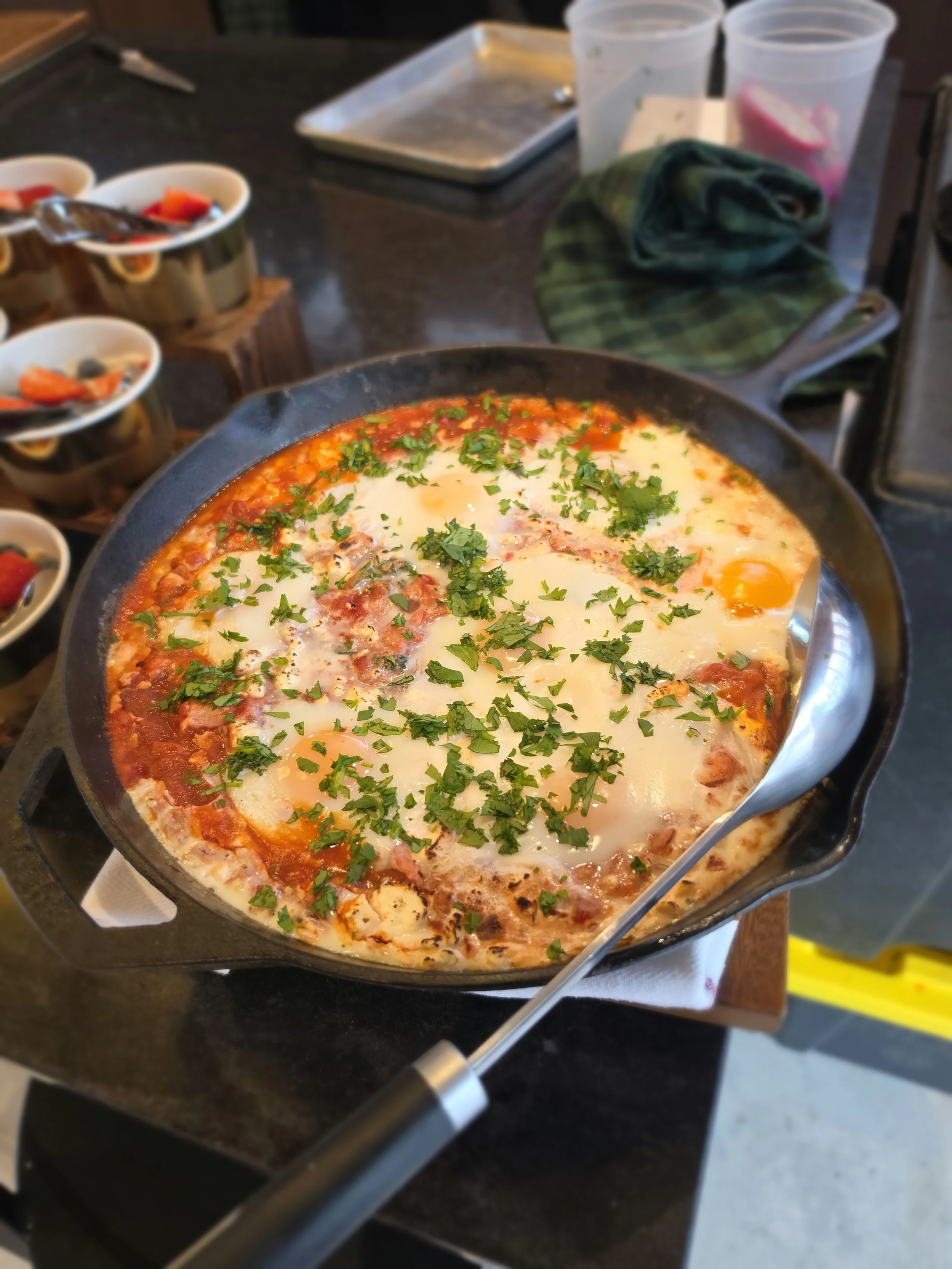 Fried eggs and chopped herbs in a black skillet on a stove in a kitchen.