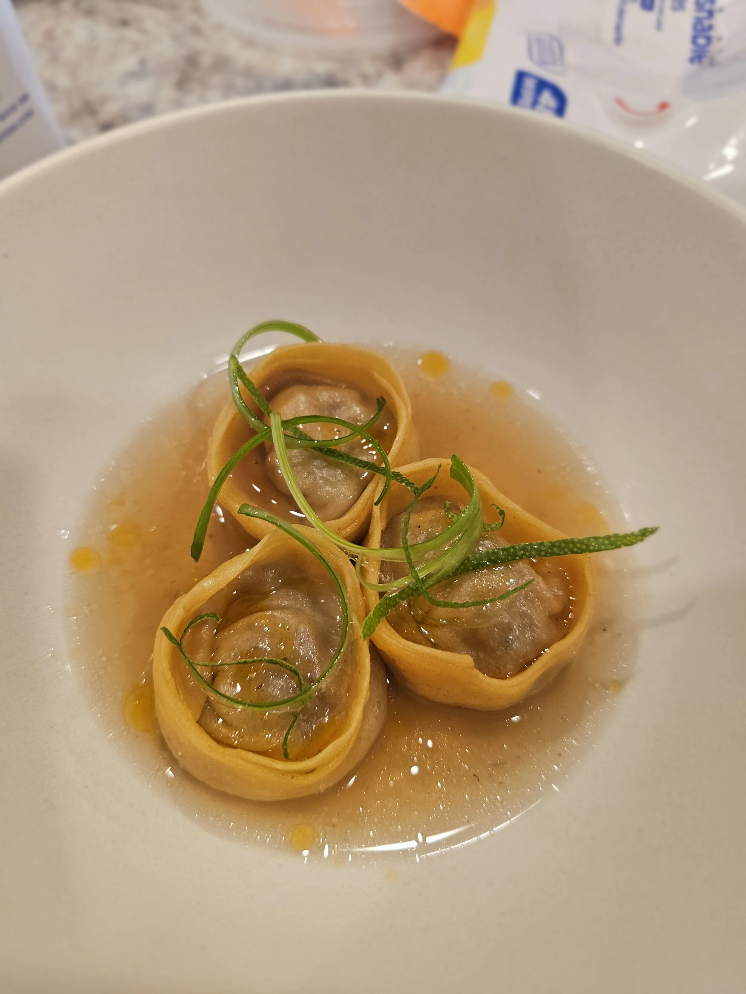 Close-up of three tortellini pasta with green herb garnish in broth on a white bowl.