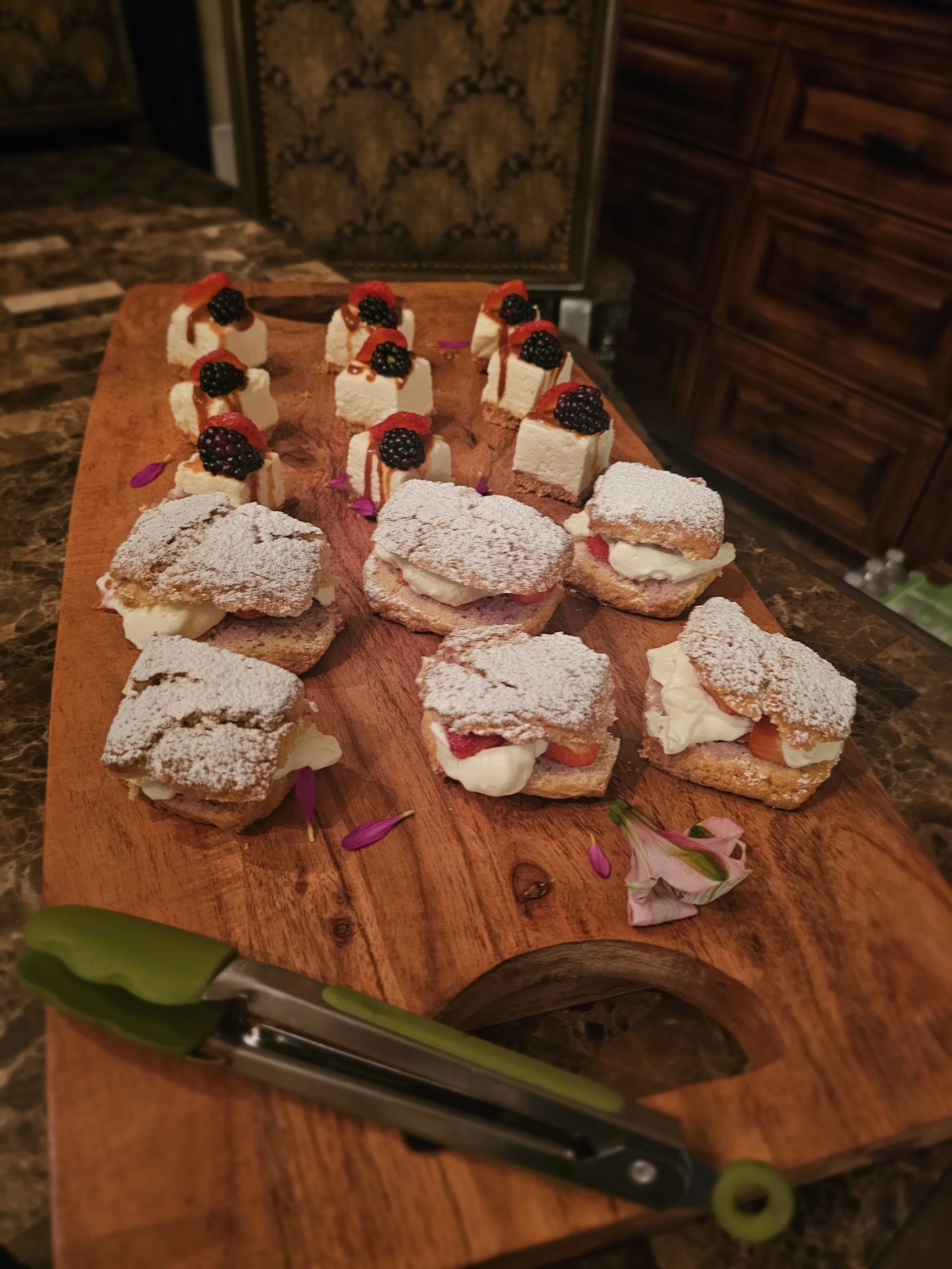 Assorted pastries and small cakes decorated with berries and powdered sugar on a wooden serving board.