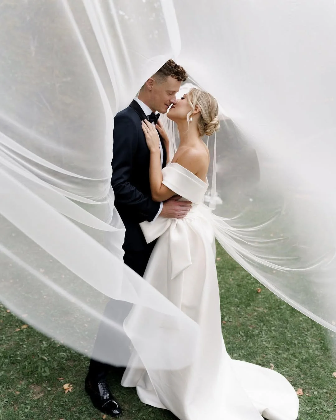Bride and groom embracing under flowing white fabric outdoors