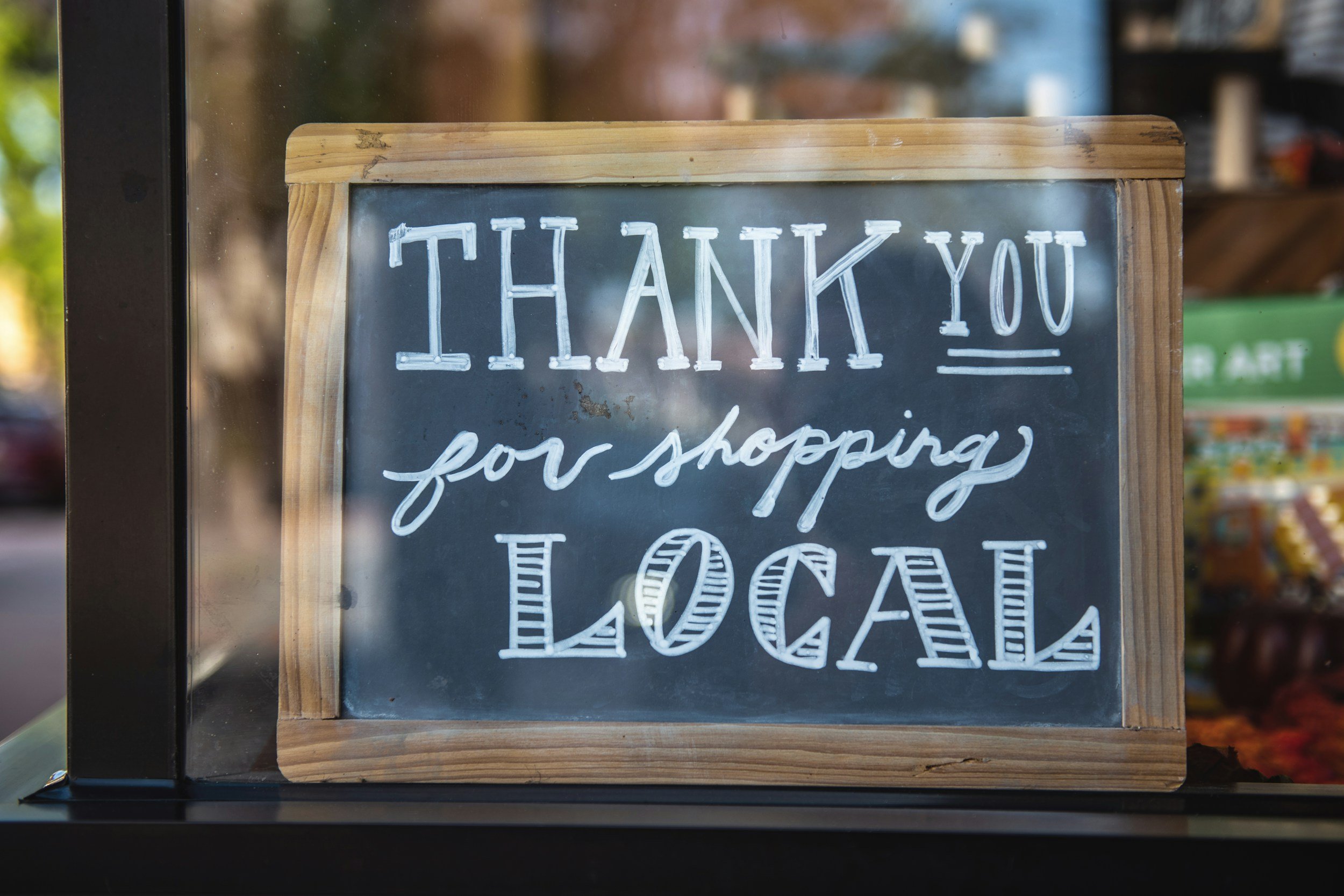 A chalkboard sign with a wooden frame displaying the words 'THANK YOU for shopping LOCAL' hand written in white chalk.