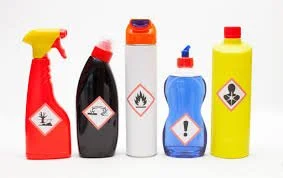 Five bottles of cleaning chemicals with hazard labels, including flammable, toxic, and corrosive symbols.
