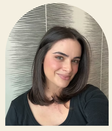 A woman with shoulder-length dark hair taking a selfie in front of a patterned wall.