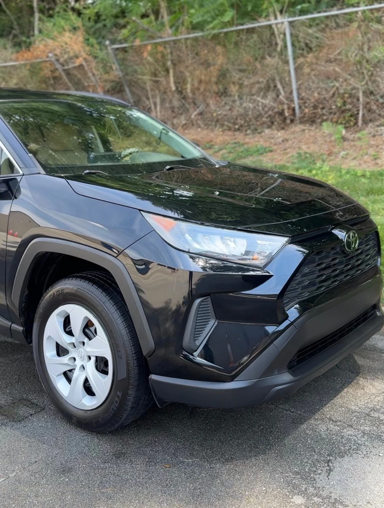 A black Toyota SUV parked on asphalt with a chain-link fence and trees in the background.