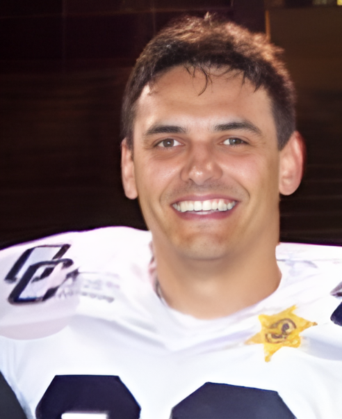 Young man smiling in a sports jersey, likely a football player, with a star-shaped patch on his shoulder, in an indoor setting.