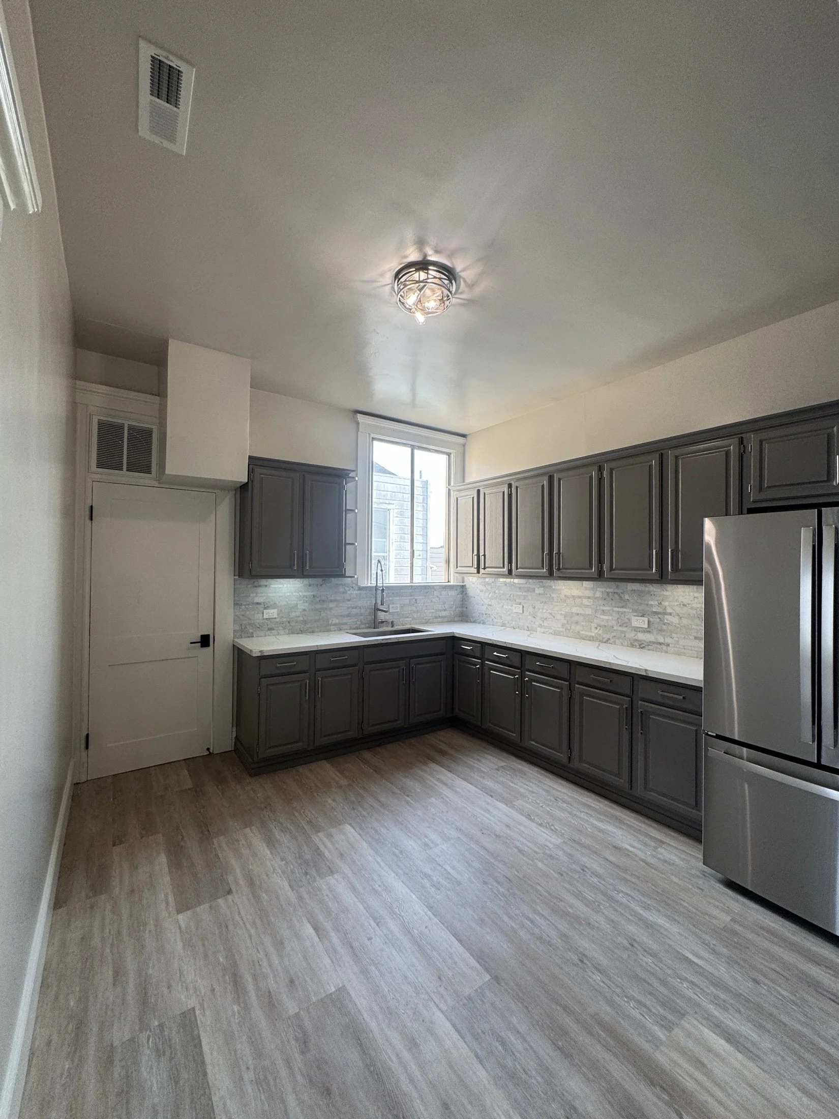 Kitchen with gray cabinets, white marble countertops, stainless steel appliances, and a window above the sink, with laminate flooring.