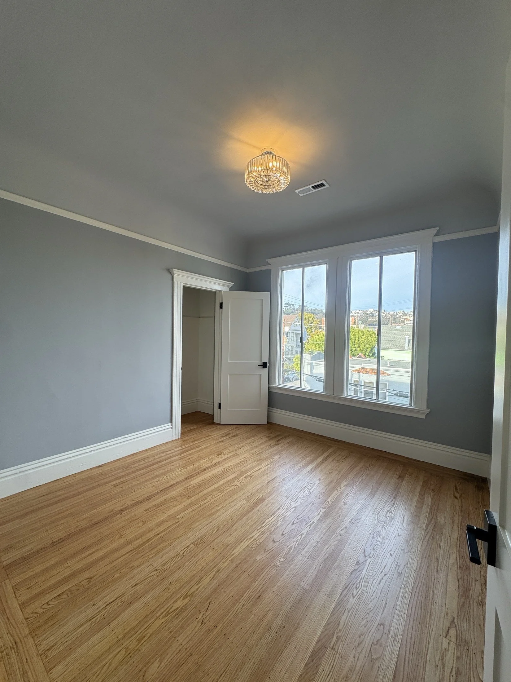 Empty room with hardwood flooring, a large window, a closet with open door, and a chandelier on the ceiling.