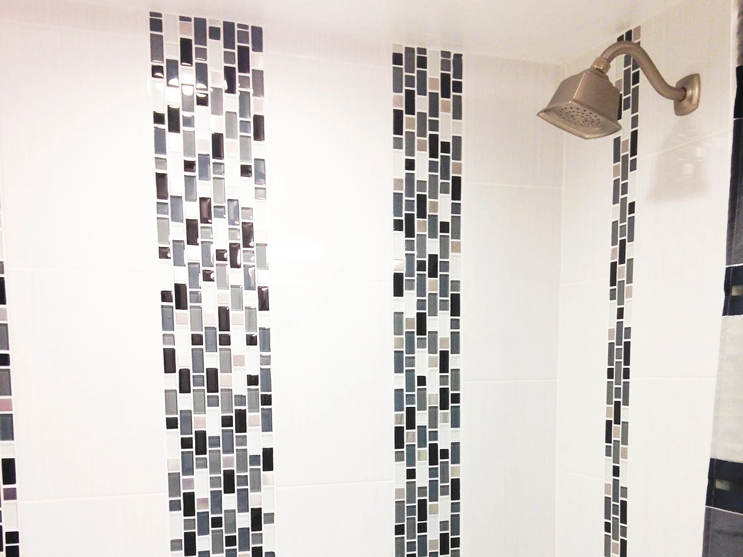 Bathroom shower with white and black mosaic tile accents and a silver showerhead.