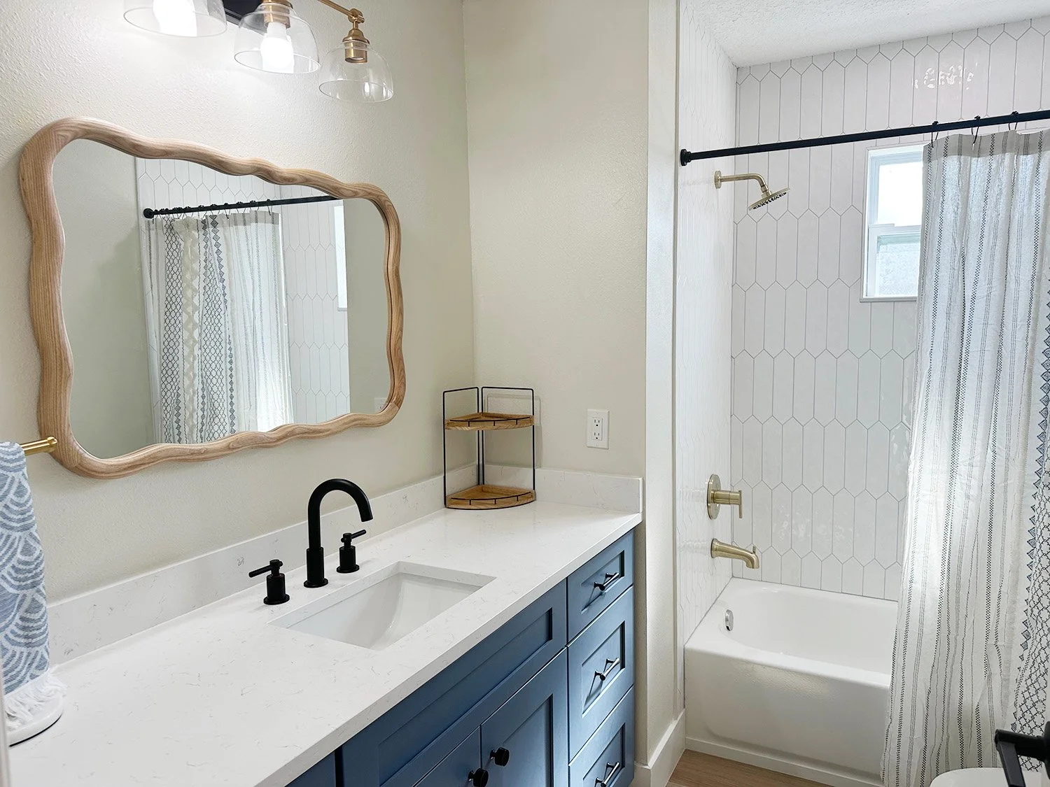 Bathroom with white walls, a large mirror with a wooden frame, black fixtures, blue vanity, and a bathtub with a shower curtain.