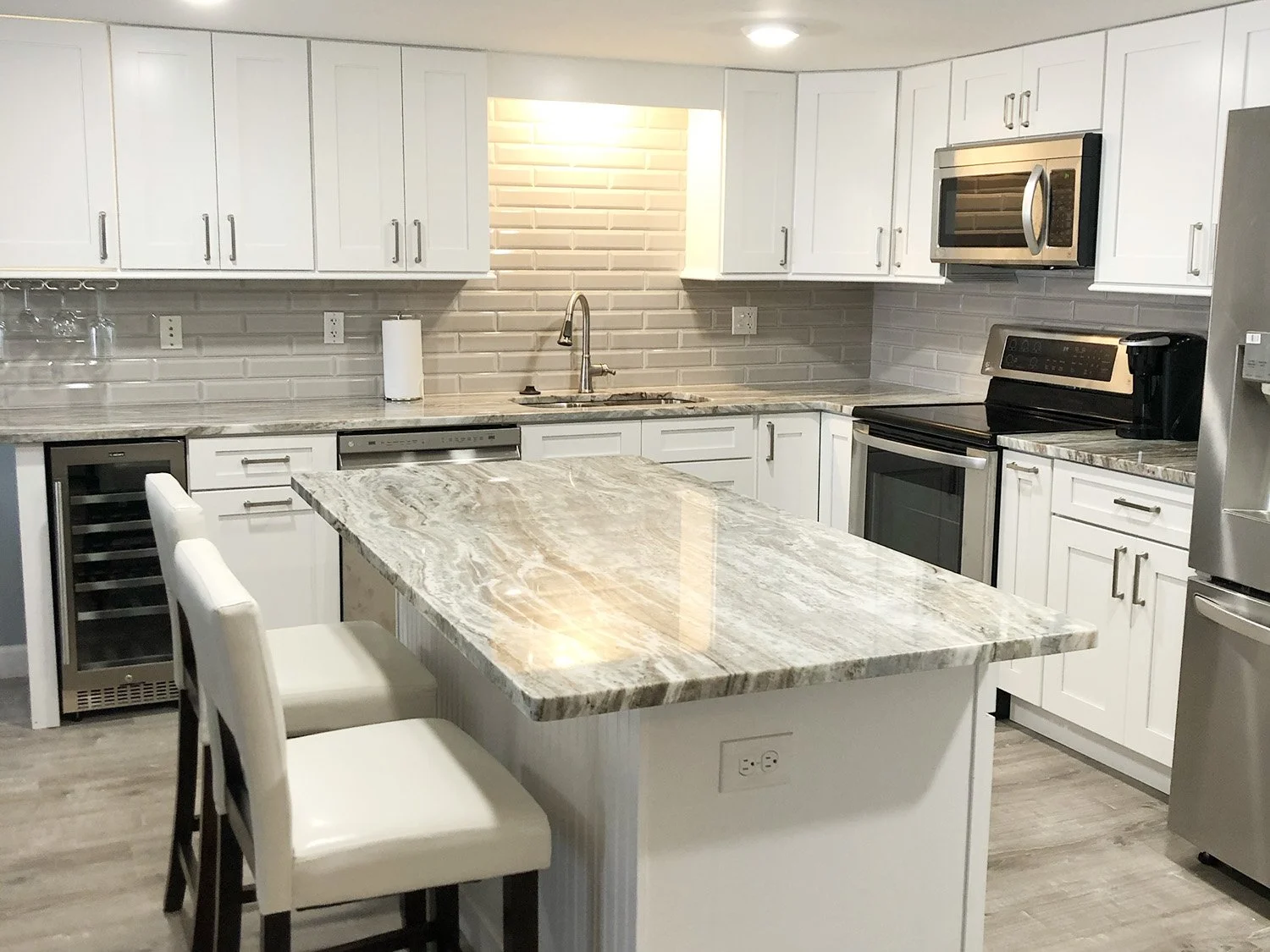 Modern kitchen with white cabinets, granite countertops, stainless steel appliances, a kitchen island, and seating for two.