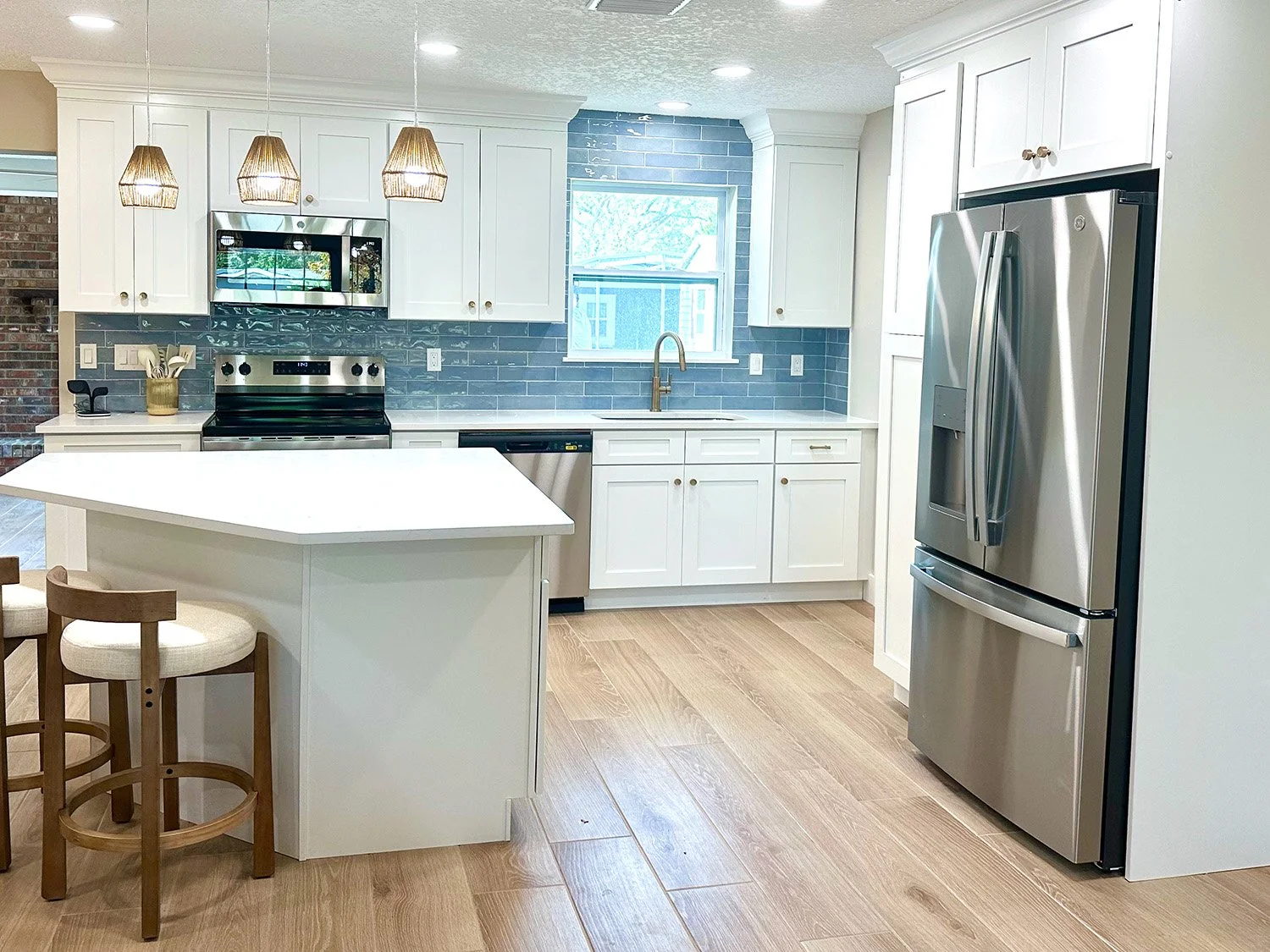 Modern kitchen with white cabinets, gray tile backsplash, stainless steel appliances, light wood flooring, and a small breakfast bar with two wooden chairs.