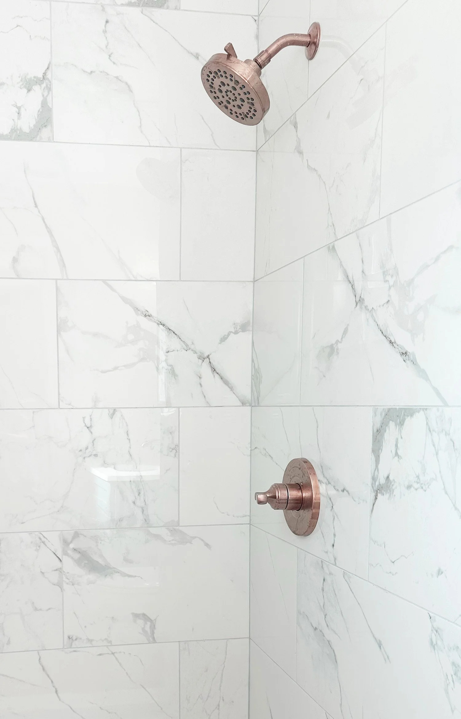 A shower head with a copper finish mounted on a marble wall in a bathroom shower.