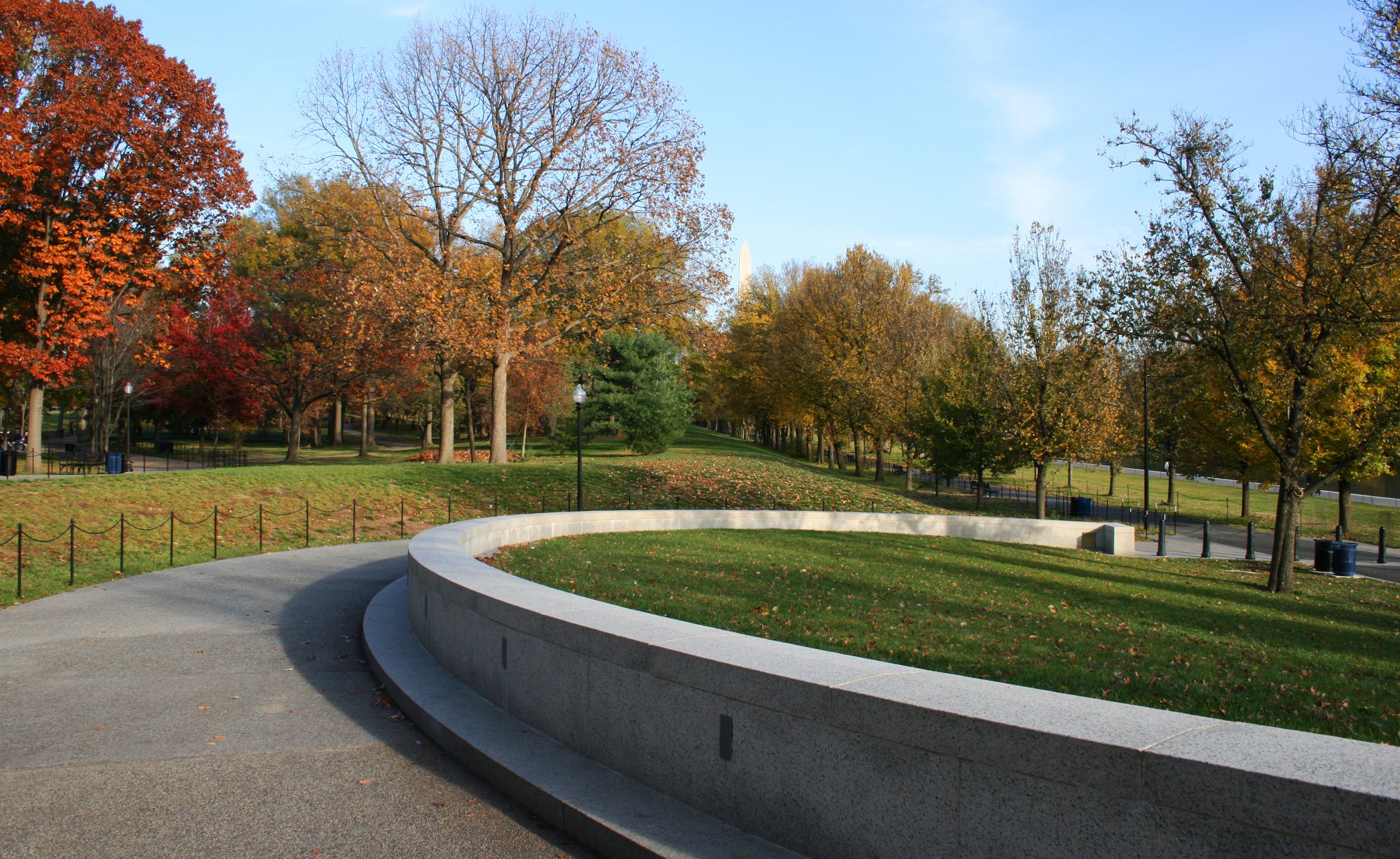 A park with colorful autumn trees, a curved concrete bench, and a paved walking path during daytime.