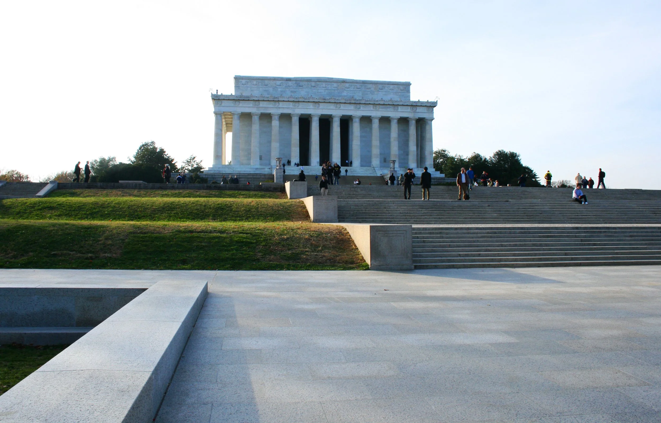 The Lincoln Memorial in Washington D.C., viewed from the steps leading up to it, with people walking and sitting around on a clear day.
