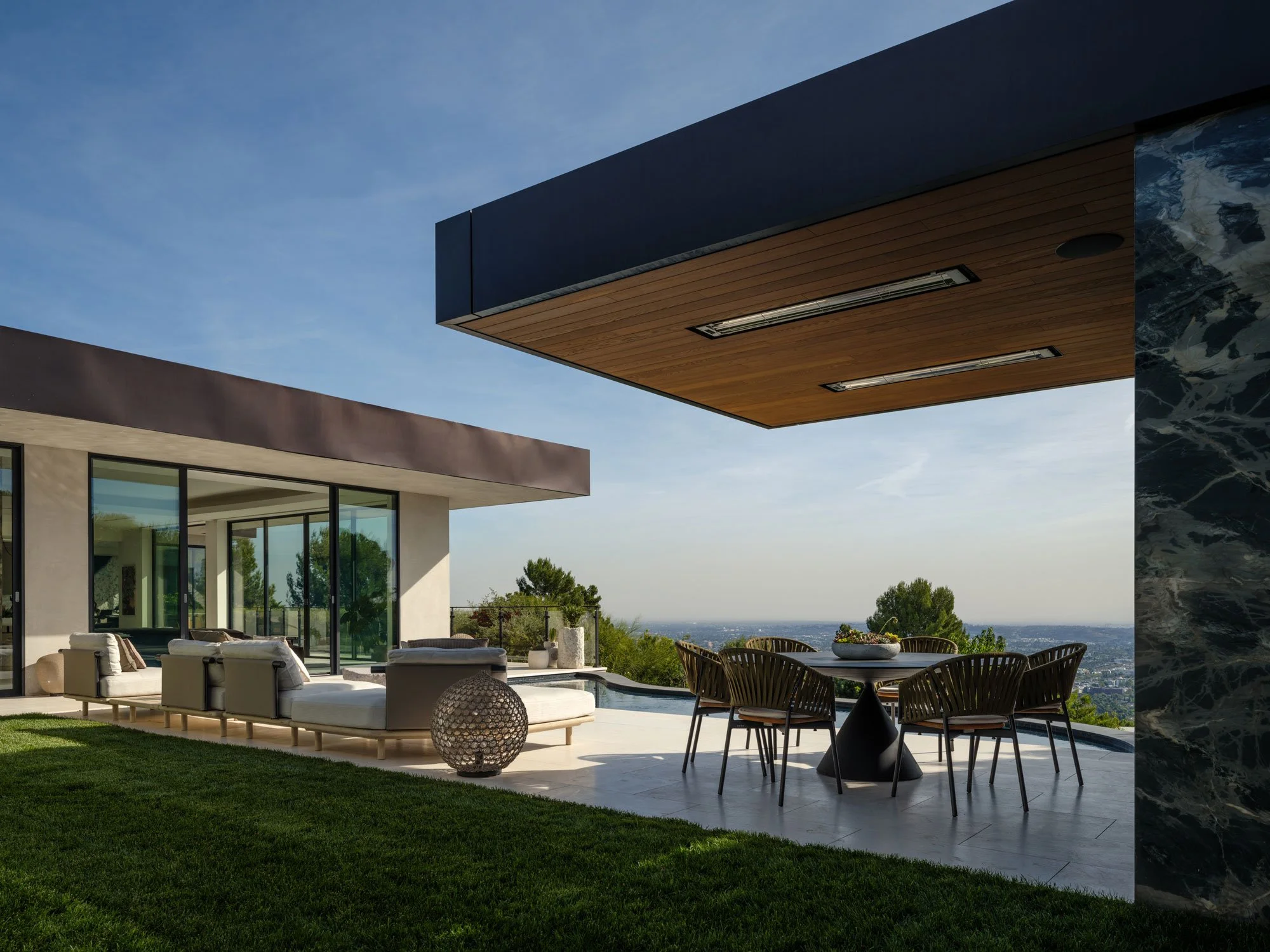 Modern house with an outdoor patio area featuring seating, a dining table, and a view of a distant horizon with trees and sky.