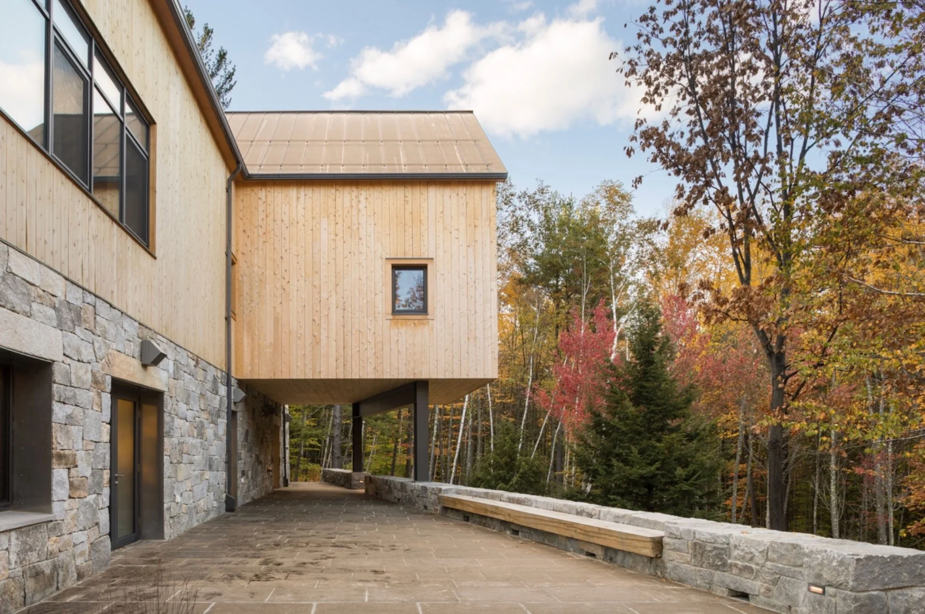 A modern house with stone and wood exterior surrounded by trees with autumn foliage.