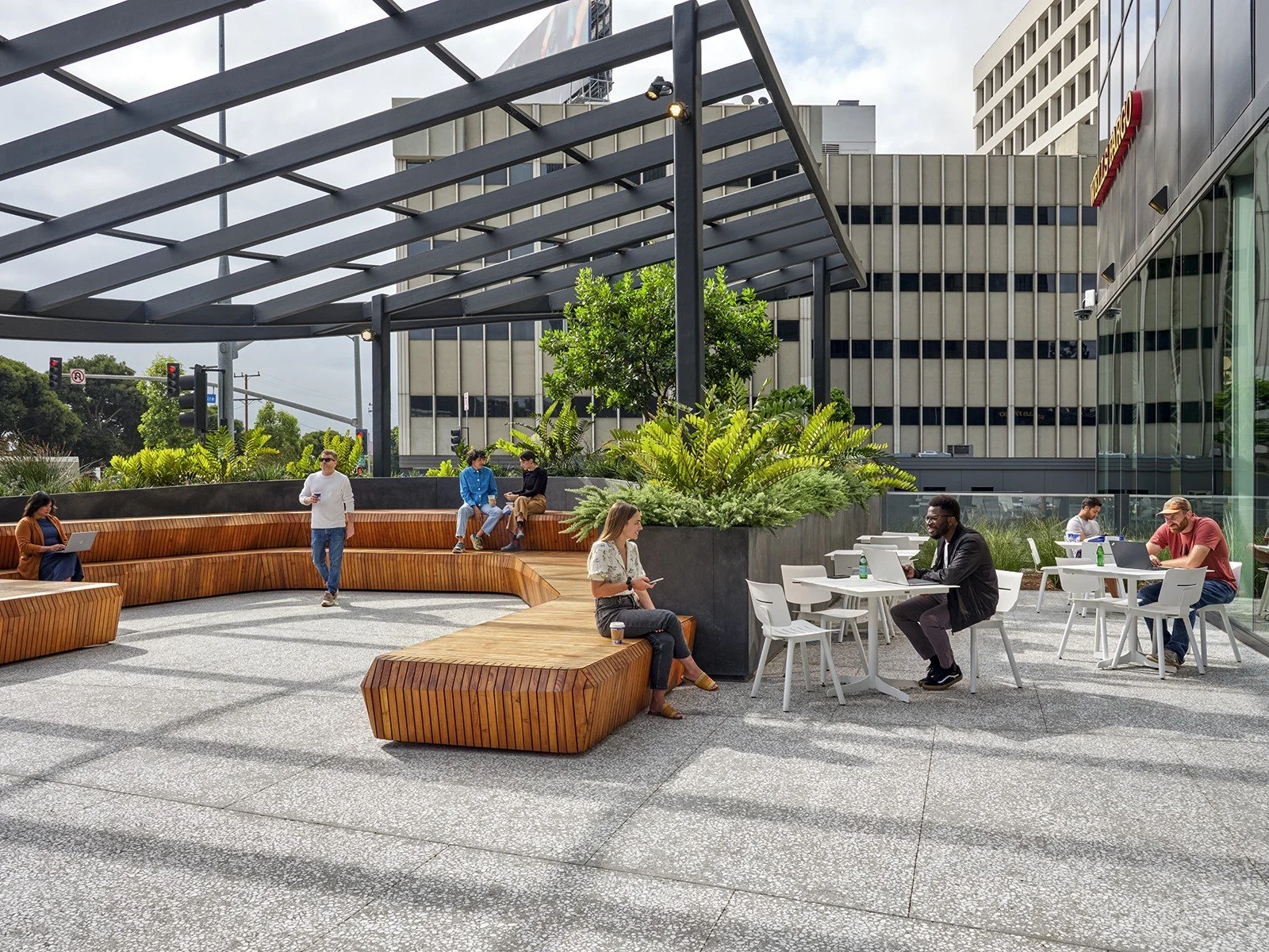 People working and relaxing on an outdoor terrace in an urban setting with modern architecture and greenery.
