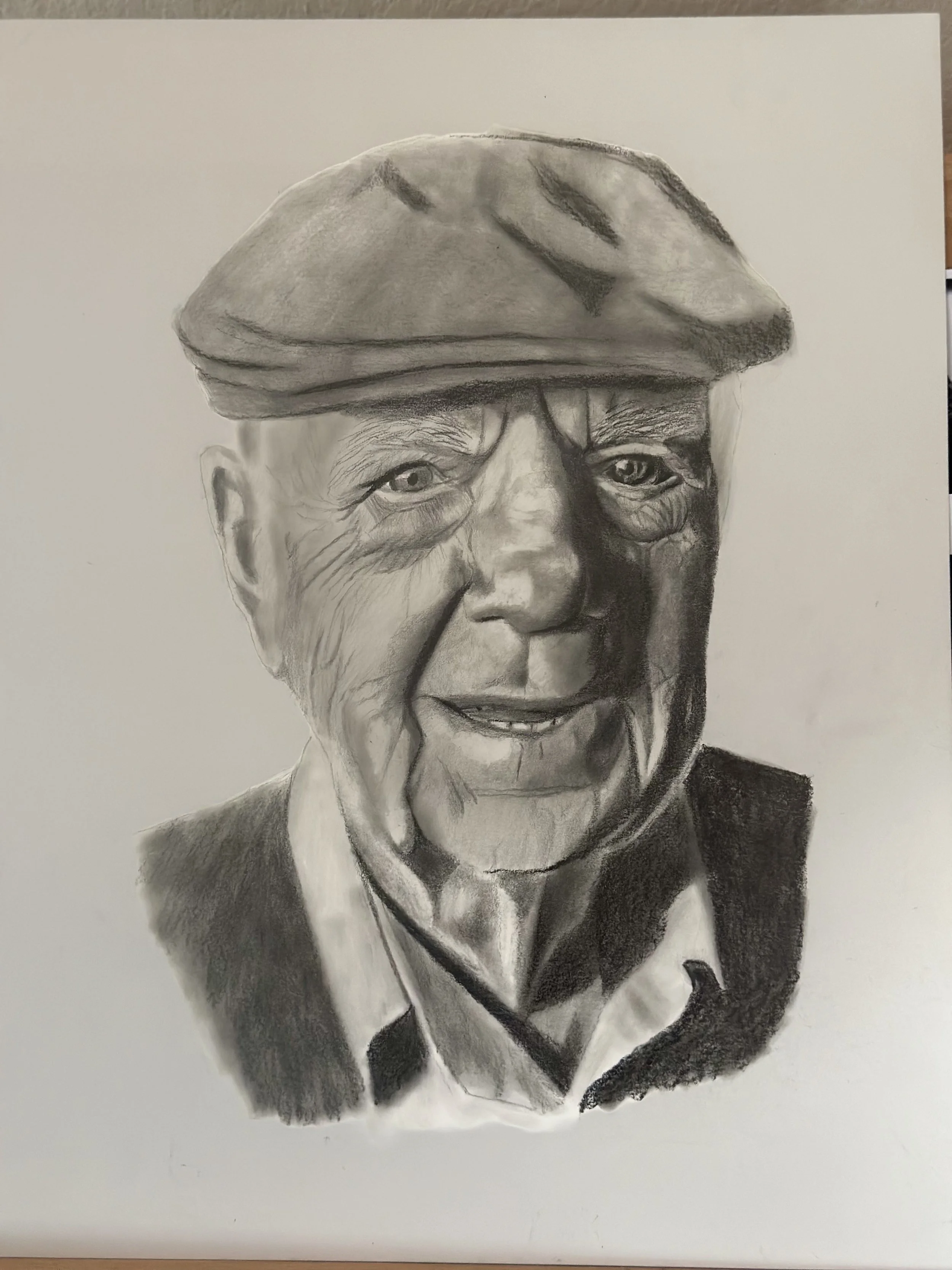 A realistic black and white pencil drawing of an elderly person wearing a cap and a collared shirt.