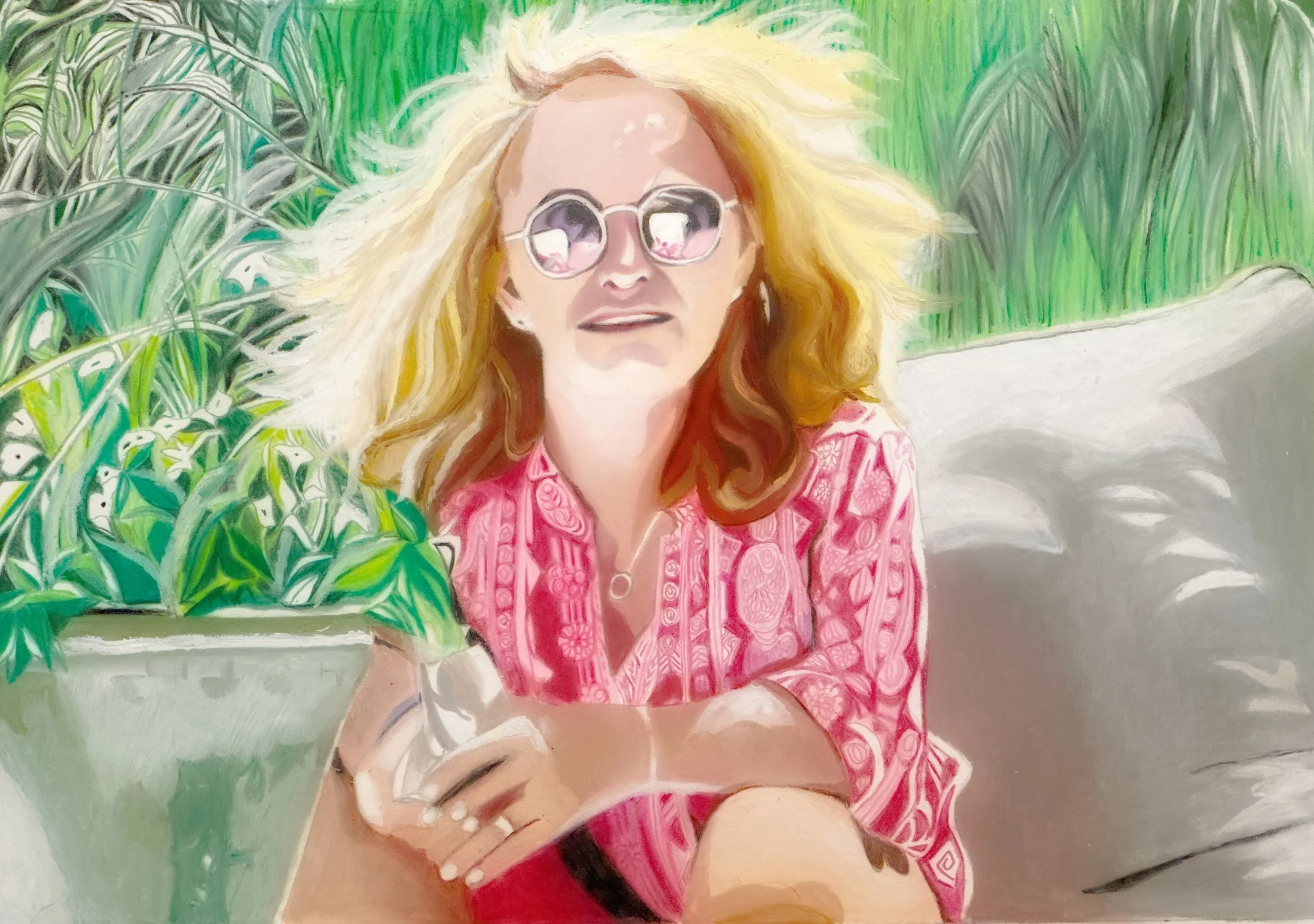 A woman with blonde hair and sunglasses taking a selfie outdoors surrounded by green plants, wearing a pink patterned top.